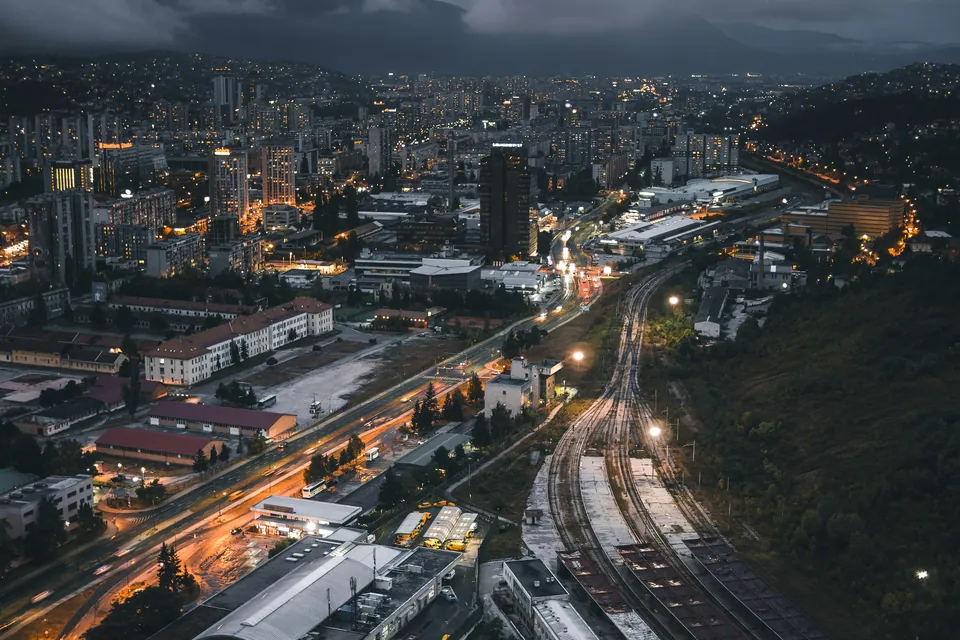 Una ciudad al anochecer, calles iluminadas y vías de tren al pie de las colinas