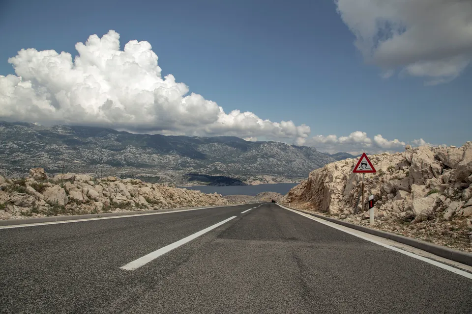 An open road through rocky hills with the sea beyond